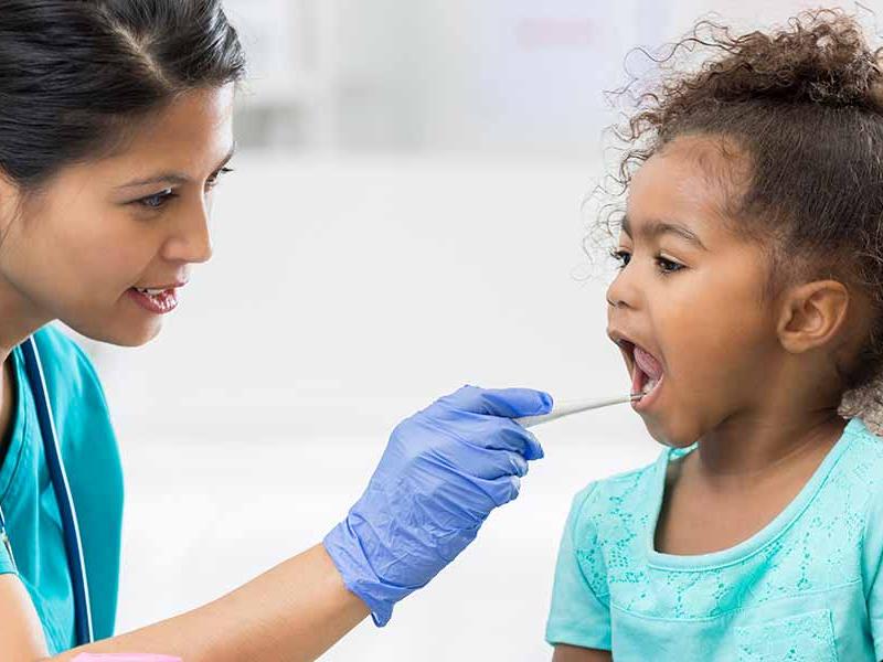Female pediatrician uses a thermometer to check a young female patient's temperature.
