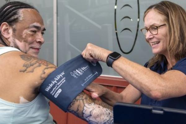 A man receives a blood pressure screening from a woman. Both smile.
